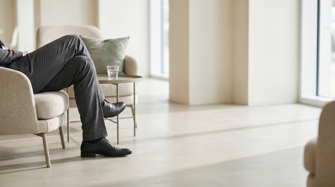 A person's crossed legs while seated in an armchair in a bright minimal lounge — editorial photograph.